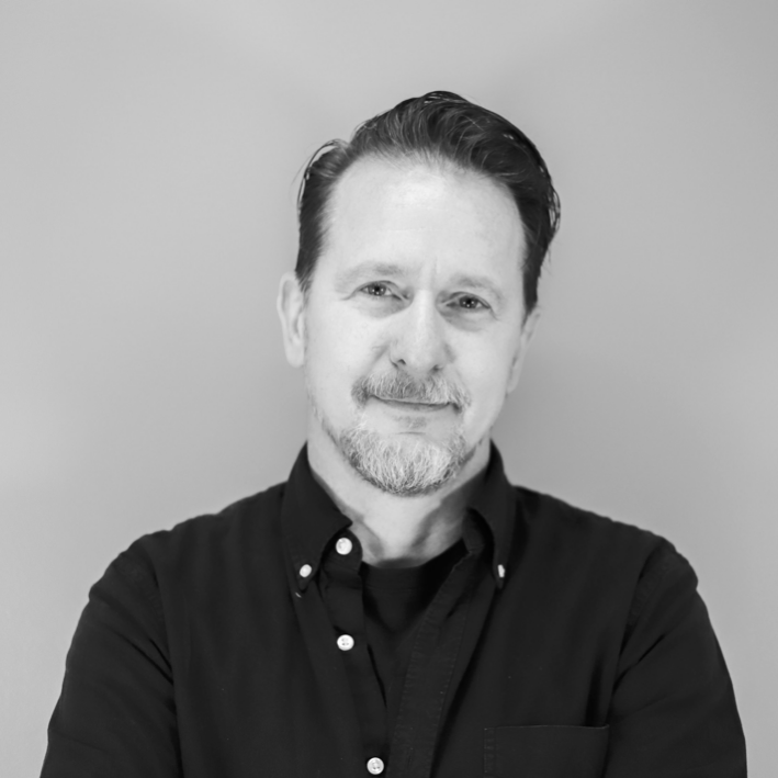 Portrait of a man with brown hair and glasses on a flat gray background.